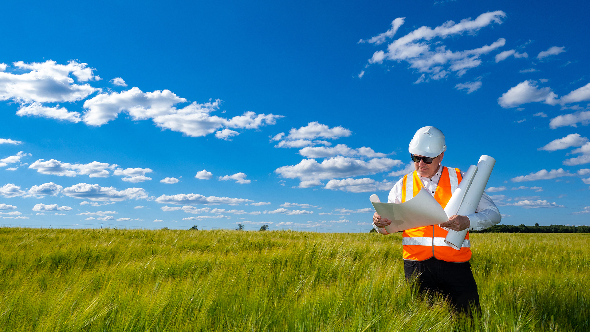 Man architect. Architect with papers on summer field. Man in construction worker uniform. Architect reviews construction drawings. Concept - choice of territory for construction of residential area